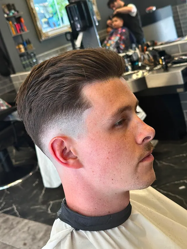 A side-parted cut with a skin fade, styled and finished, in profile